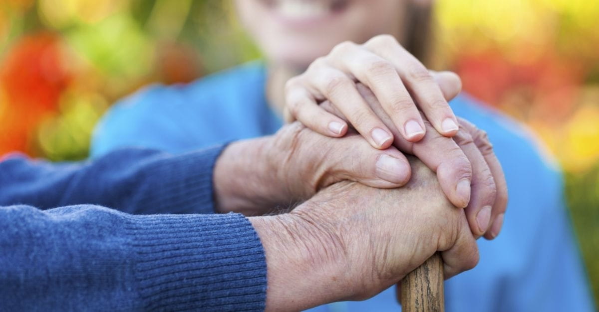 A woman's hands rest on the hands of an older individual.